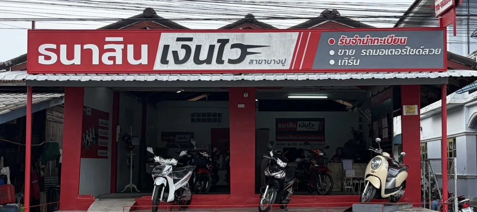 หน้าร้านธนาสินเงินไว สาขาบางปู อำเภอยะหริ่ง จังหวัดปัตตานี ป้ายร้านสีแดง มีมอเตอร์ไซค์มือสองจอดหน้าร้าน